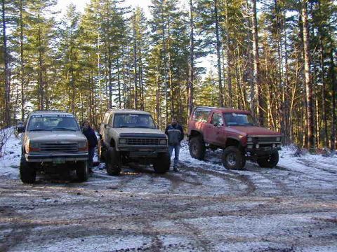 1994 Ford Explorer - Three off-road vehicles are parked in a wooded area with snow on the ground.
