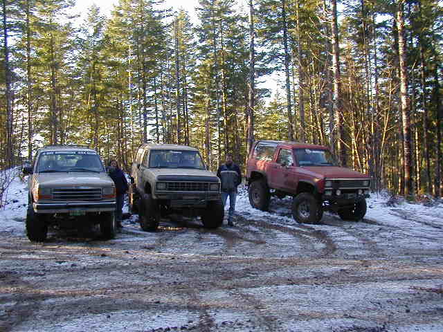 Three lifted 4x4s in snowy forest: tan Bronco, tan Bronco II, red Blazer