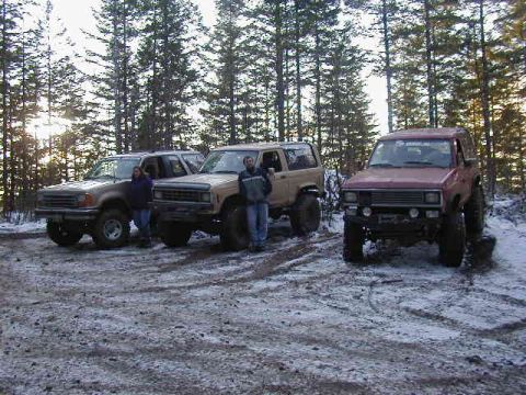 1994 Ford Explorer - Three SUVs are parked in a snowy forest clearing with tall pine trees in the background.