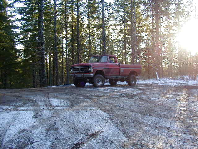 Lifted red Ford F-series 4x4 pickup on a snowy dirt forest road, side view
