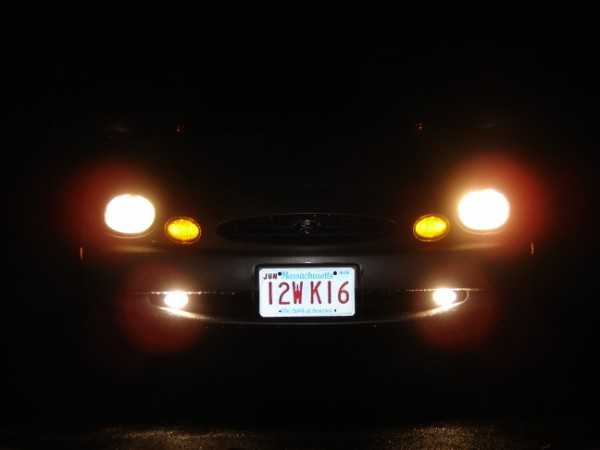 Front of a dark car at night with headlights and fog lights on, white Massachusetts plate reading 12WK16