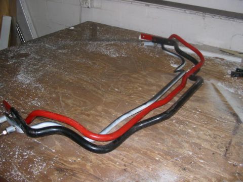 1985 Ford Crown Victoria LTD - Three automotive sway bars are laid out on a workbench, with a watermark indicating the source as Supermotors.net.