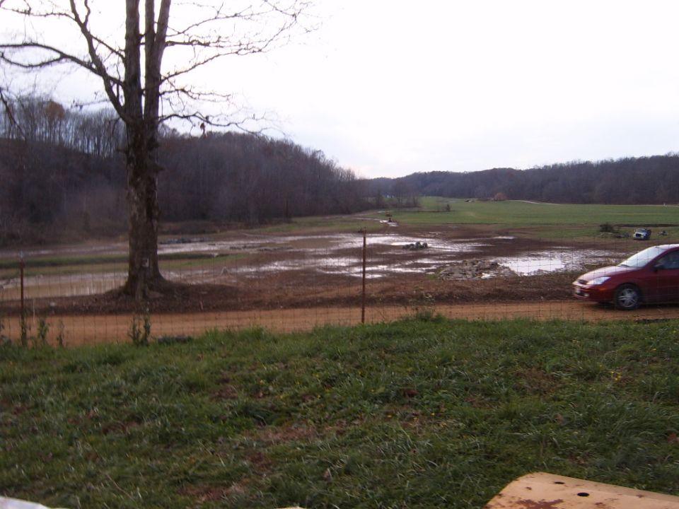 Red sedan parked on a dirt road next to a muddy field