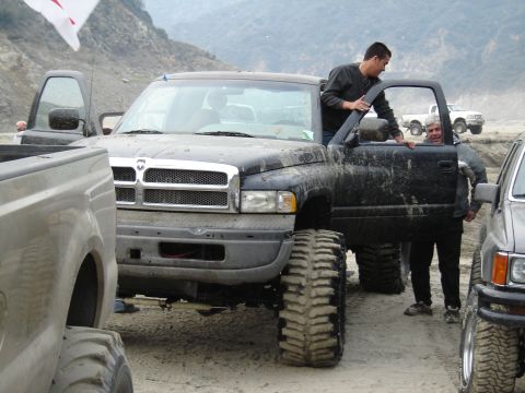 2000 Ford F-450 - A lifted black Dodge Ram pickup truck is parked in a muddy, outdoor setting with several people around it.