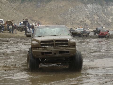 2000 Ford F-450 - Muddy Dodge Ram pickup truck navigating a challenging off-road terrain with other vehicles present.