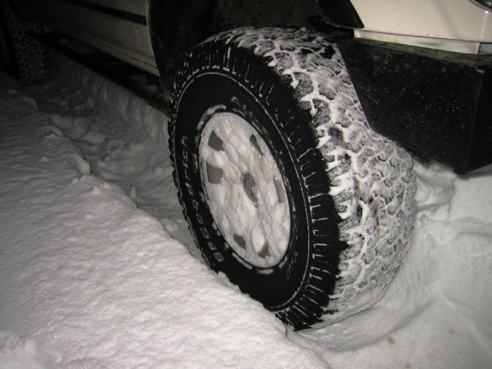 Close-up of a tire covered in snow, with the vehicle's running board visible