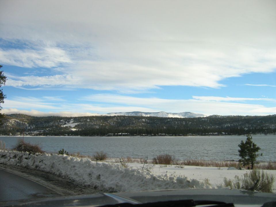 snowy landscape with a lake and mountains under a cloudy sky