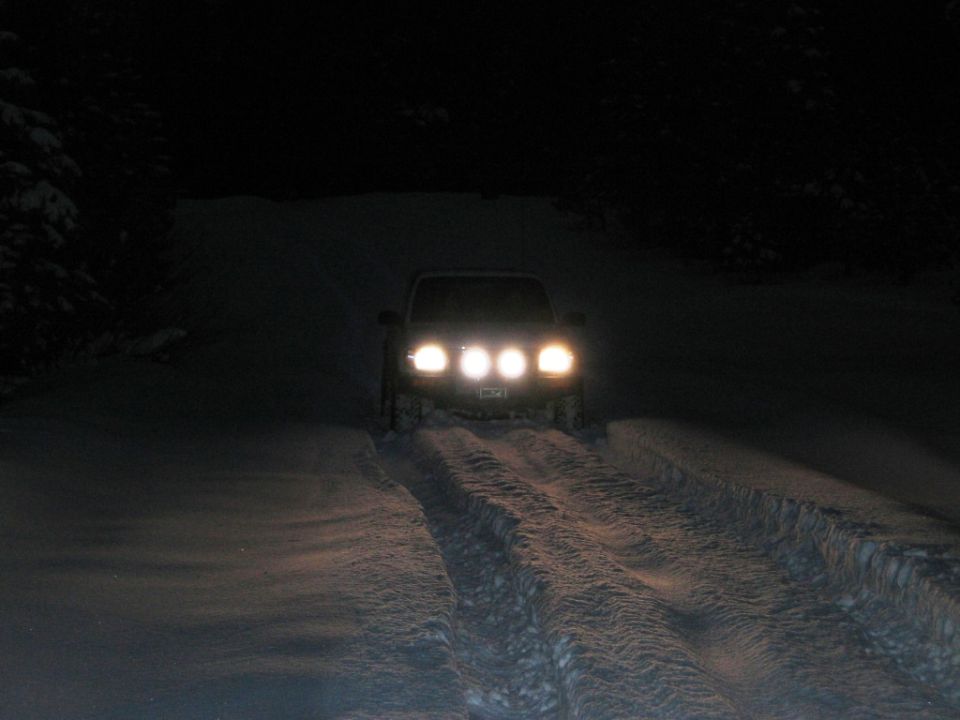 Truck with four headlights driving on a snow-covered road at night