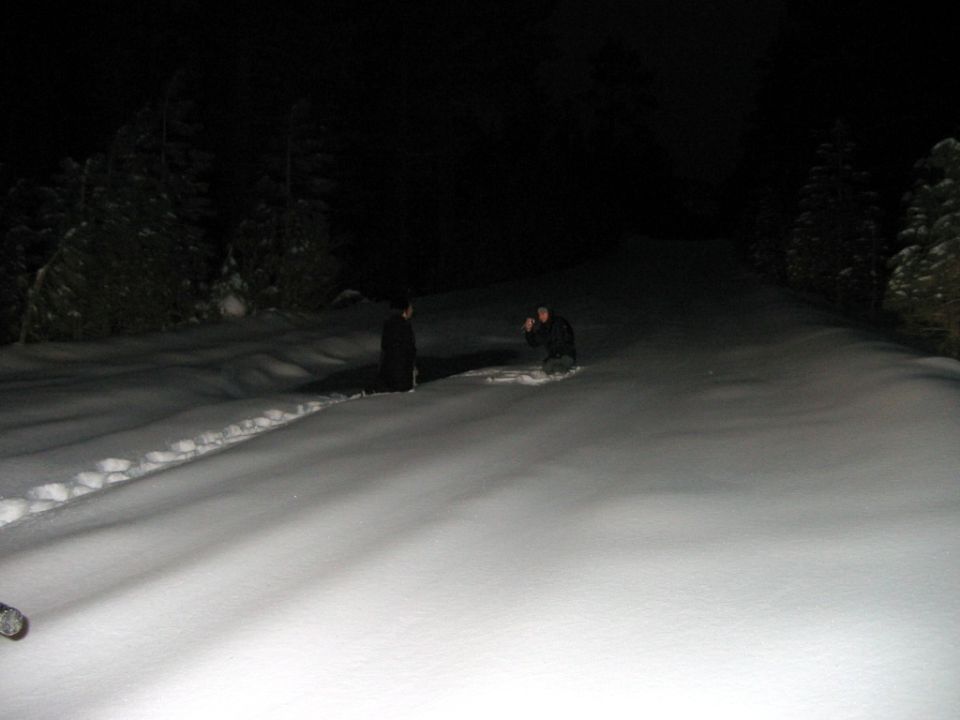 Two people in a snowy landscape at night, one kneeling and taking a photo