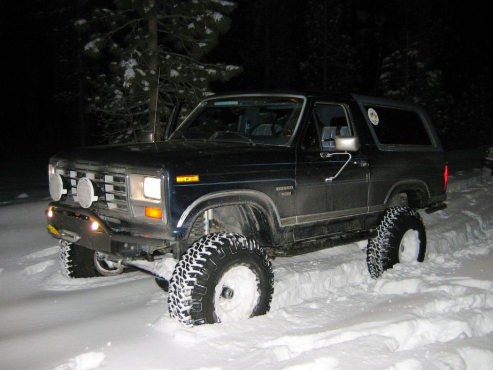 Dark blue Ford Bronco with lifted suspension and large tires in snow, front 3/4 view