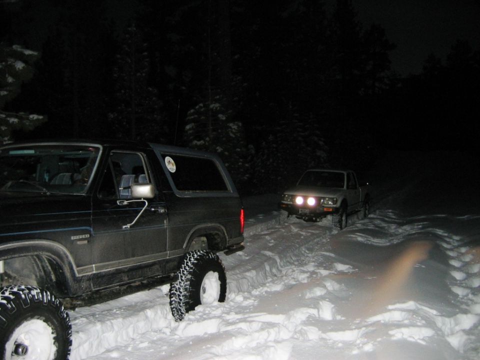 Two trucks stuck in snow at night, one in foreground, one in background with headlights on