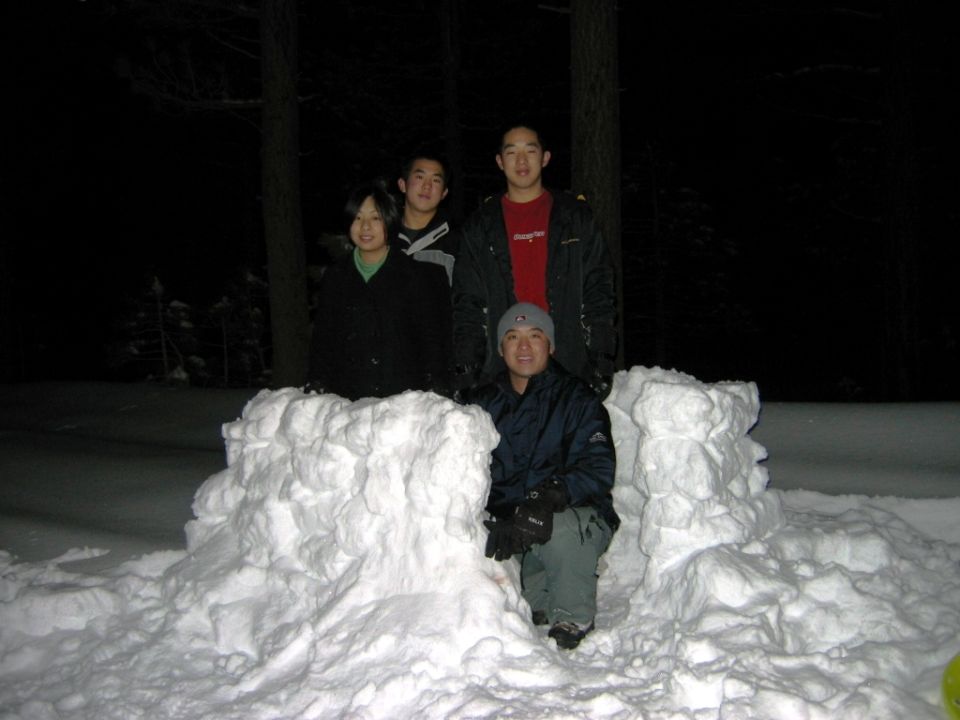 Four people pose behind a snow fort at night