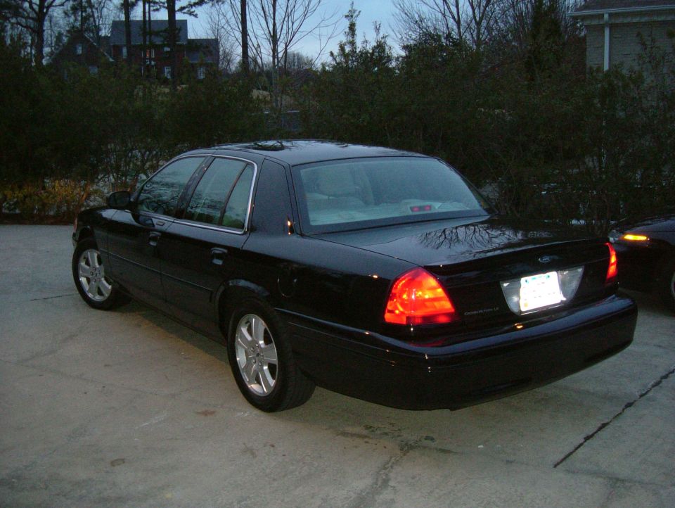 Black Ford Crown Victoria sedan rear three-quarter view parked on gravel with brake lights on