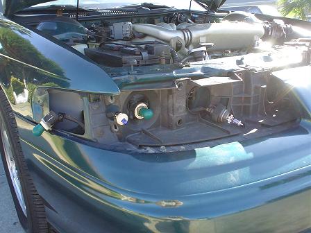 1993 Ford Taurus - Front view of a green 1993 Ford Taurus with the headlight removed, revealing the engine bay and internal components.