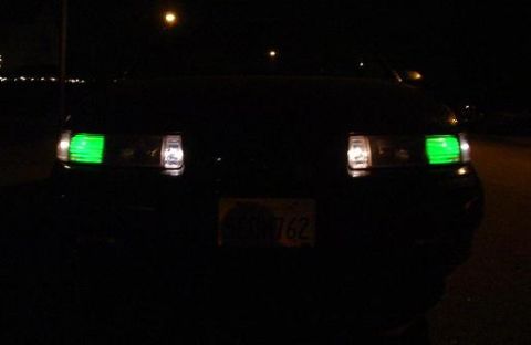 1993 Ford Taurus - 1993 Ford Taurus with custom green headlights and a license plate visible at night.