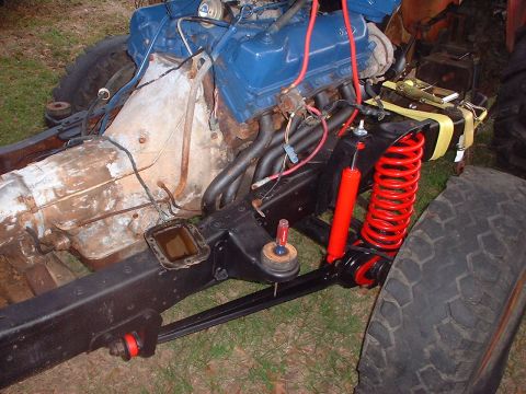 1976 Ford F-150 - Close-up of a Ford V8 engine and chassis parts, showing red shocks and springs, with visible rust on the transmission.