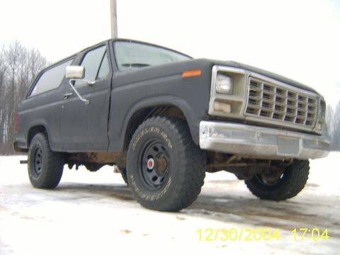 1985 Ford Bronco - A dark-colored Ford Bronco is shown from a low angle on a snowy surface, with trees in the background.