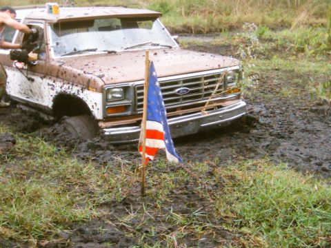 1995 Ford Bronco - This Ford truck is deeply stuck in mud, with an American flag stuck in the ground next to it.