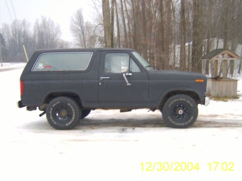 1985 Ford Bronco - A matte black Ford Bronco is parked on a snowy surface with trees in the background.