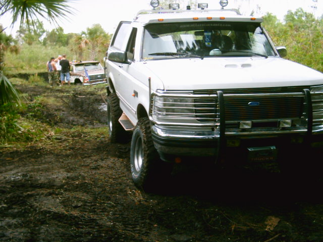 White lifted Ford Bronco with brush guard and roof lights on a muddy palmetto trail