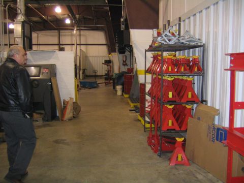 1978 Ford Bronco - A man stands in a workshop aisle lined with shelves of red jack stands and other equipment.