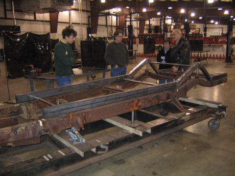1978 Ford Bronco - A group of people look at a rusty vehicle frame being worked on in a workshop.