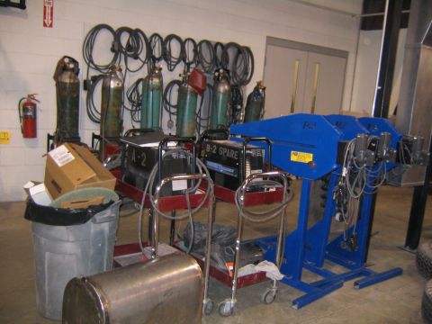 1978 Ford Bronco - Workshop scene with welding equipment, gas cylinders, and a blue fabrication machine.