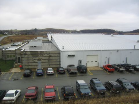 1978 Ford Bronco - A variety of vehicles are parked in the lot outside a large industrial building.