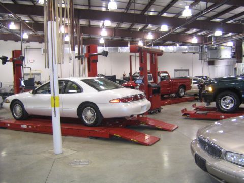 1978 Ford Bronco - Multiple vehicles are present in a repair shop, with a white coupe on a lift in the foreground.