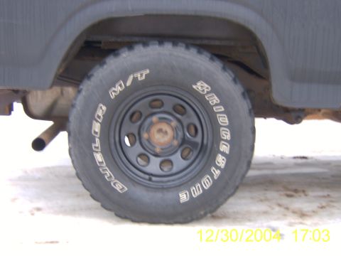 1985 Ford Bronco - A close-up view of a truck's tire and wheel well, showing tire brand details and part of the vehicle's body.