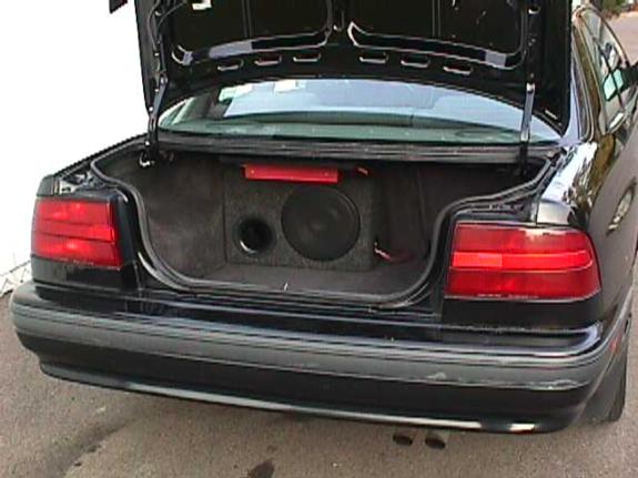 Open trunk of a black sedan with a single subwoofer enclosure mounted against the rear seat