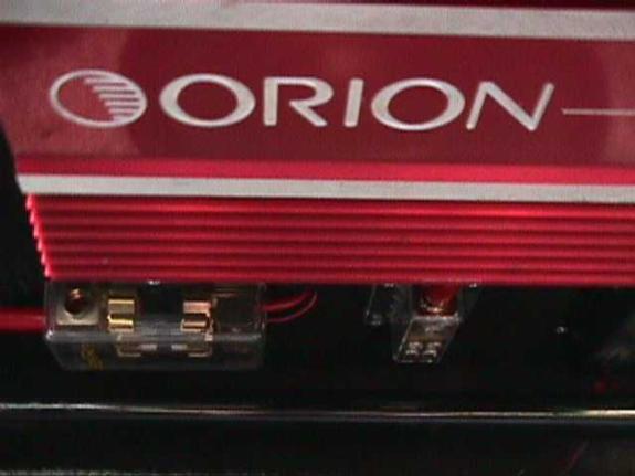 Red Orion car amplifier close-up with logo, heatsink fins, and gold wiring terminals