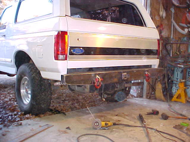 Rear of a tan Ford Bronco on a lift in a garage showing differential and rear bumper with tow hooks