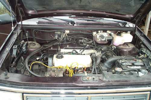 Open engine bay of a vehicle showing inline engine, reservoirs, and wiring with hood raised