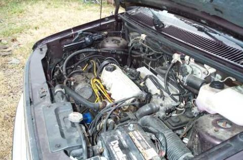 1988 Ford Bronco - The engine bay of a vehicle is shown, various hoses, wires, and a battery. A watermark for SUPERMOTORS is visible.