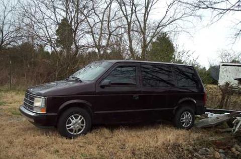 1988 Ford Bronco - A dark minivan is parked on a grassy area with trees in the background. The vehicle appears to be from the mid-1980s.