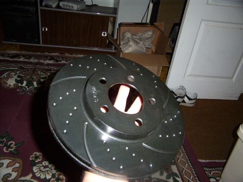 1998 Mercury Sable - A close-up view of a perforated and slotted brake rotor held by a hand.