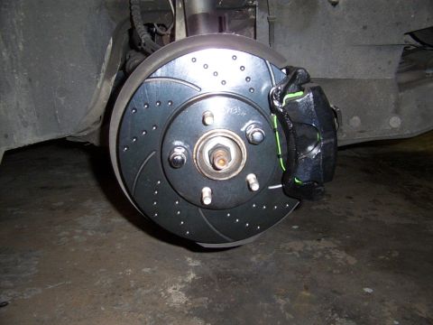 1998 Mercury Sable - Close-up of a drilled and slotted brake rotor and black caliper with green accents, likely an aftermarket upgrade.