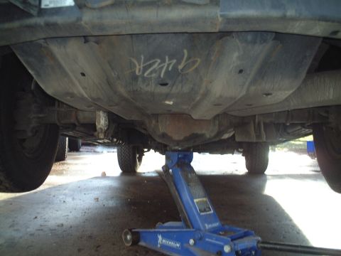 2000 Ford Excursion - Underbody view of a large SUV supported by a blue hydraulic jack, with '942R' marked on a panel.