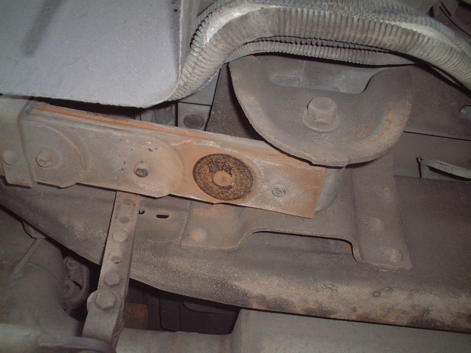 Rusty underbody frame crossmember with bolts and corroded circular plate