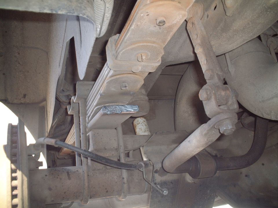 Undercarriage view of leaf spring suspension with U-bolts, shock, and duct tape, covered in dust.