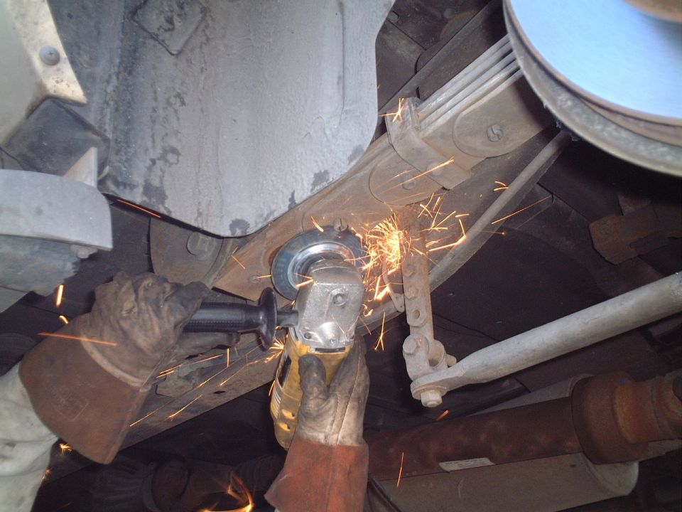 Angle grinder cutting a bolt on a leaf spring suspension, spraying sparks under a vehicle