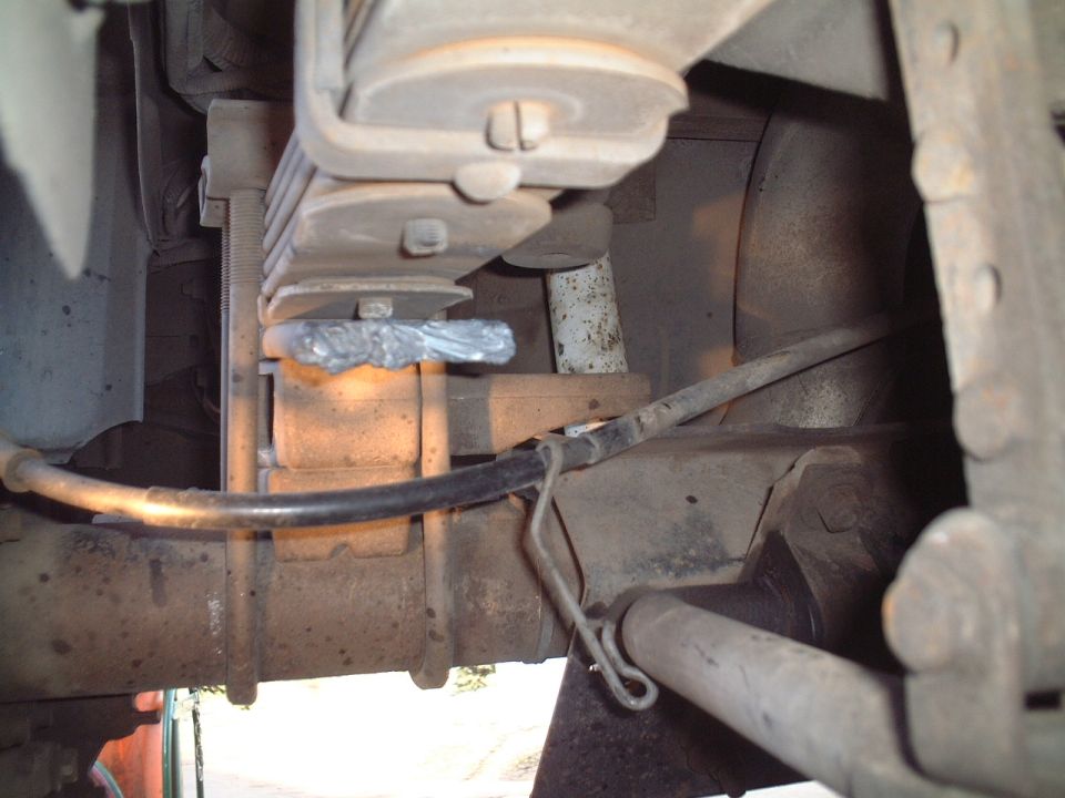 Underside of leaf spring suspension with rusty axle, U-bolts and rubber line