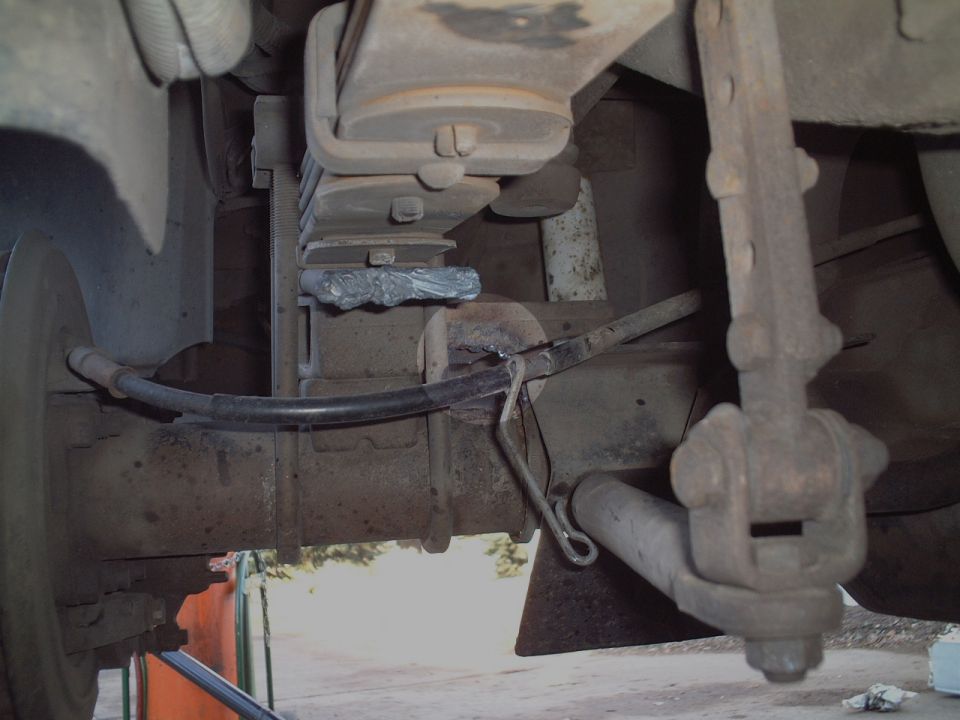 Rusty rear leaf spring, axle and shock absorber viewed from underneath a vehicle