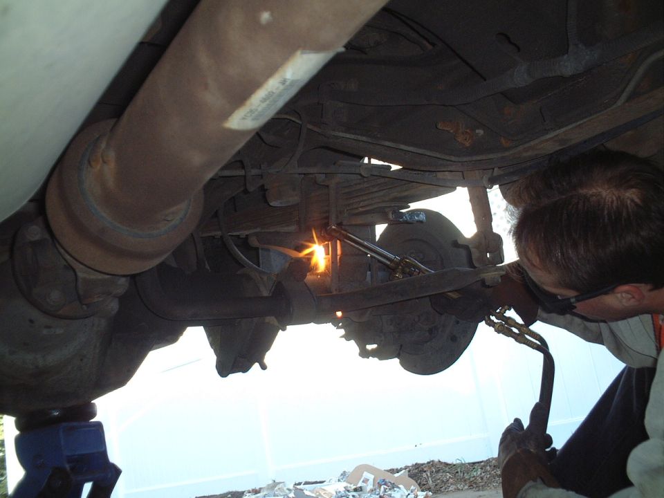 Man with torch working under vehicle chassis near rear suspension and brakes