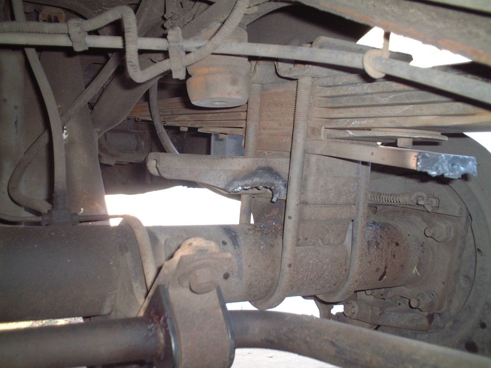 Undercarriage view of rear leaf spring, solid axle and brake drum, dusty and rusty