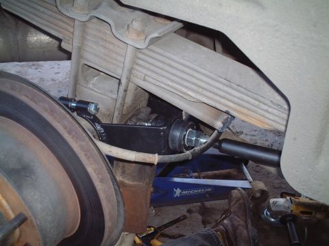 2000 Ford Excursion - Installation of a suspension component on the rear axle of a vehicle, with a jack and tools present.