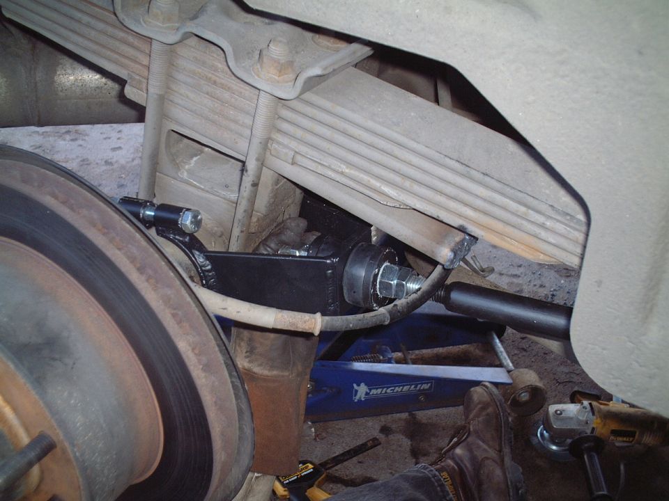 Rear leaf-spring suspension with new black shock and bracket, brake rotor, and tools underneath vehicle