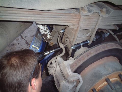 2000 Ford Excursion - A mechanic works on the rear suspension of a 2000 Ford Excursion, focusing on the leaf springs and brake assembly.