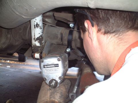 2000 Ford Excursion - Mechanic works on the undercarriage of a vehicle, using an impact wrench and other tools.